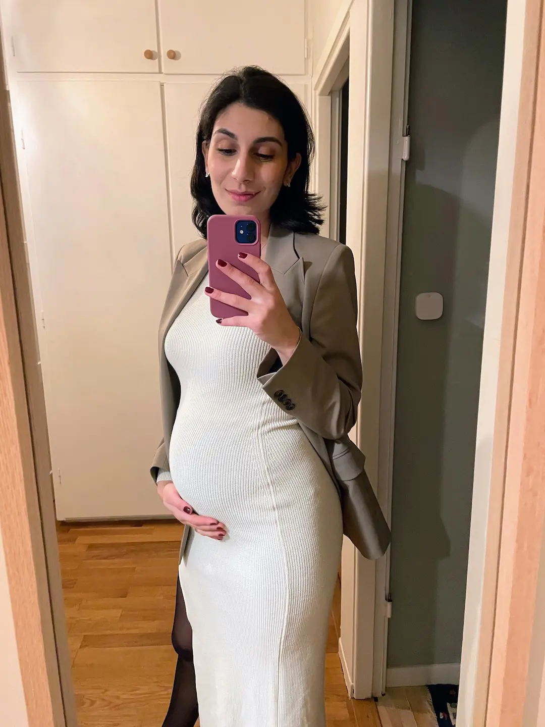 Gravid person i ljus våroutfit med lager i varm hemmamiljö.