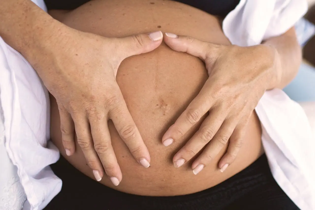 Gravid kvinna i svarta gravidkläder med händerna formade som ett hjärta mot magen.