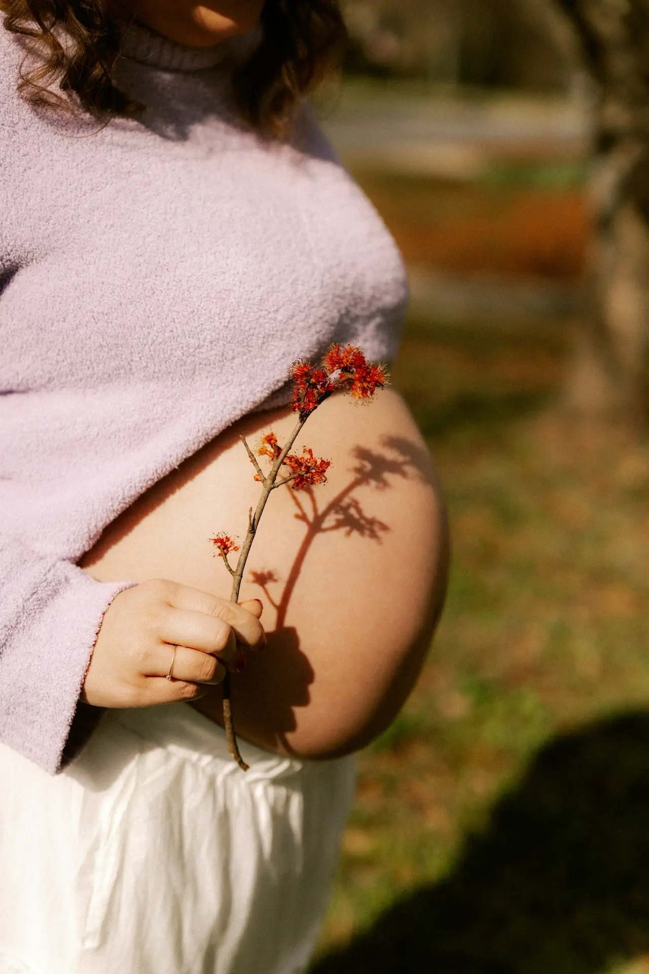 Gravid person i ljus våroutfit med lager i varm hemmamiljö.